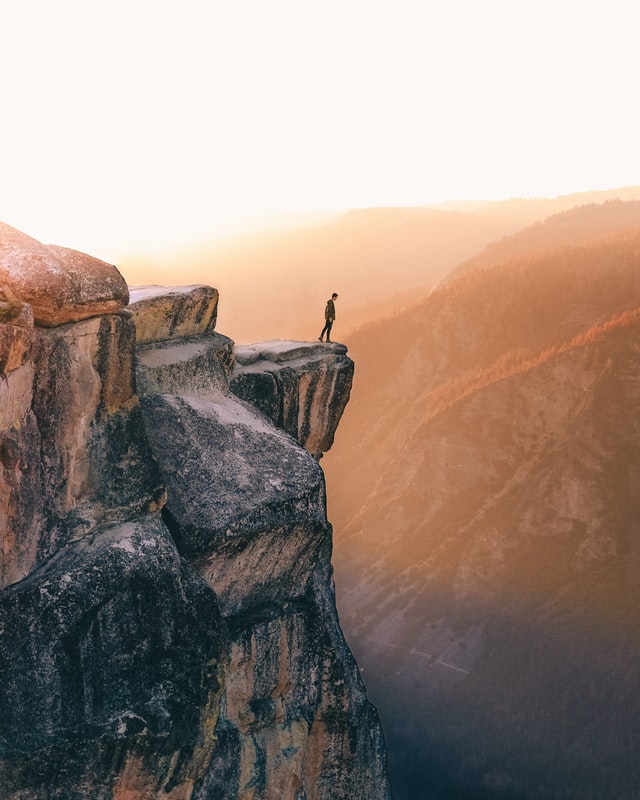 A man standing on cliff, looking at the drop